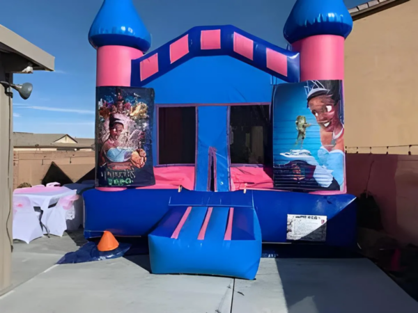 Inflatable bounce house with blue and pink castle design and Aladdin-themed panels, set up outdoors.