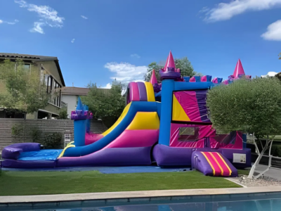 Colorful inflatable bounce house with slide next to a swimming pool in a backyard.