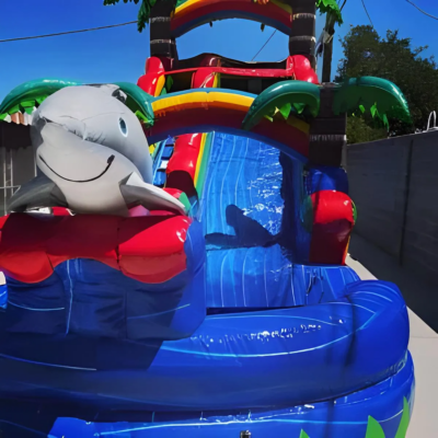 A colorful inflatable water slide with a shark design and palm trees.